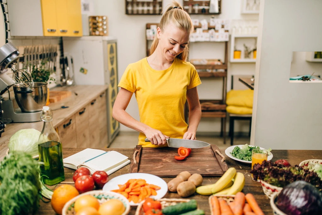 Jade Carter chopping a ripe red tomato on a wooden cutting board, surrounded by fresh vegetables for a new recipe.