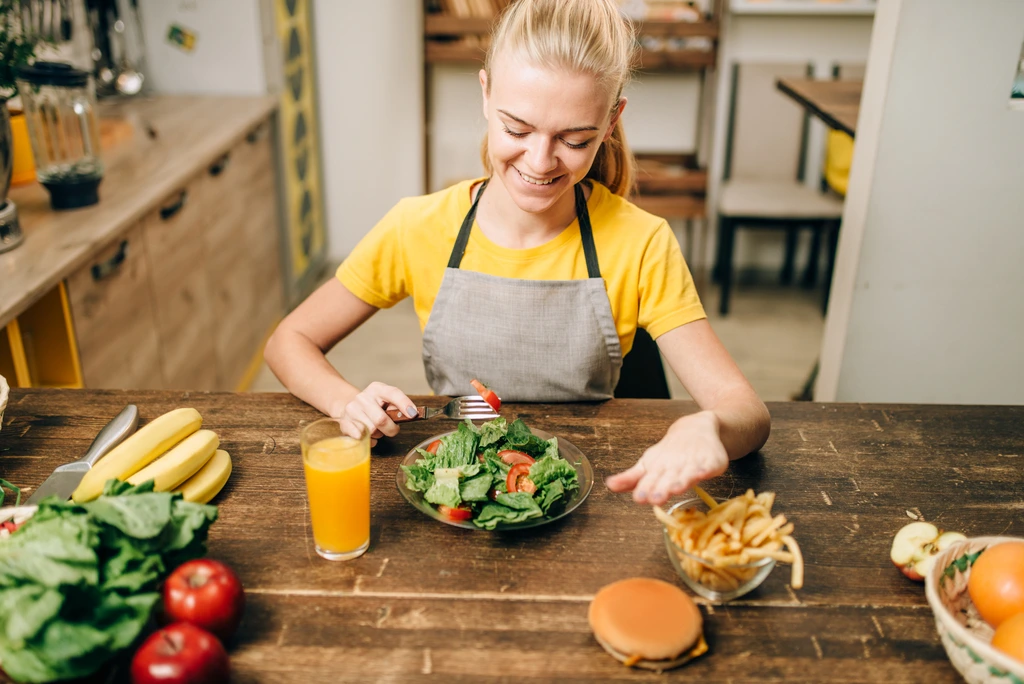 Jade Carter, founder of Cooking by Jade, smiling as she eats a fresh green salad at a rustic wooden kitchen table.