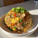 A mound of flavorful chicken fried rice with visible pieces of egg, carrots, and peas, topped with fresh green onions.