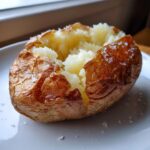A perfectly cooked air fryer baked potato, split open to show fluffy interior and crispy, salted skin.