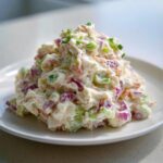 A generous scoop of creamy crab salad mixed with celery and red onion, garnished with chives.