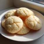 A stack of golden, slightly cracked 3-ingredient butter cookies resting on a light-colored plate near a window.