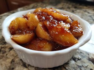 Close-up of thick, glossy, spiced apple pie filling served in a small white fluted bowl.