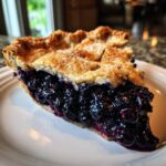 A thick slice of amazing blueberry pie recipe showing juicy filling and a golden, sugared lattice crust.