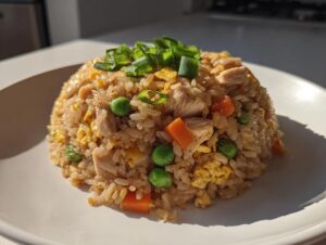 A mound of flavorful chicken fried rice featuring visible pieces of chicken, carrots, peas, and scrambled egg, topped with fresh green onions.