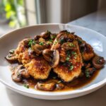 Close-up of breaded Chicken Marsala cutlets smothered in rich brown sauce and sliced mushrooms.