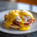 Close-up of classic eggs benedict featuring poached eggs, ham, and rich hollandaise sauce on a toasted English muffin.
