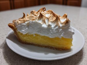 A close-up slice of lemon meringue pie showing bright yellow filling and tall, toasted meringue peaks.