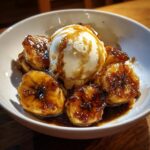 A close-up of rich, caramelized bananas foster served with a scoop of vanilla ice cream drizzled with sauce.