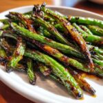 Close-up of blistered, vibrant green chinese green beans with garlic sauce on a white plate.