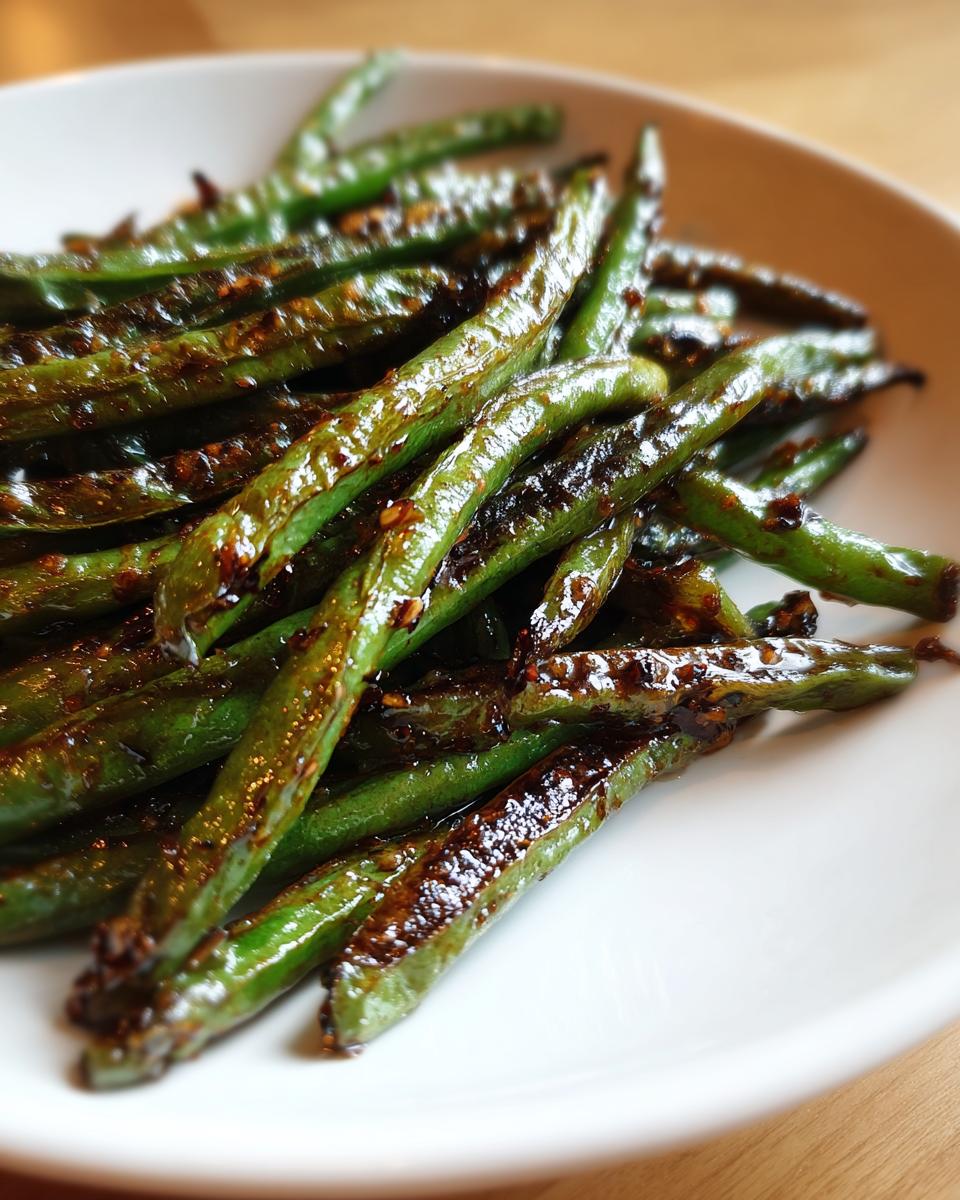 A close-up of vibrant green beans coated in a dark, glossy garlic sauce, ready to serve.
