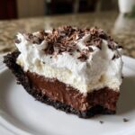 Close-up of a slice of Christmas chocolate cream pie showing dark crust, rich chocolate filling, and thick whipped cream topped with chocolate shavings.