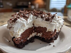 A cross-section view of a rich Christmas chocolate cream pie slice showing layers of dark crust, chocolate filling, and white whipped cream topped with shavings.