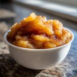 Close-up of chunky, homemade applesauce generously sprinkled with cinnamon in a small white bowl.