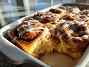 A close-up view of a freshly baked cinnamon roll casserole, drizzled heavily with white icing.