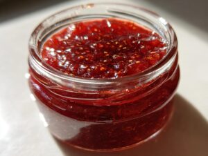A close-up of glistening, deep red homemade christmas jam filled in a small, clear glass jar.