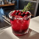 A vibrant red cranberry pomegranate margarita served over ice, garnished with fresh cranberries and rosemary.