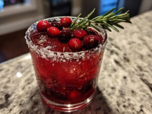 A vibrant red cranberry pomegranate margarita served in a sugar-rimmed glass, garnished with fresh cranberries and rosemary.