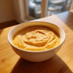 A close-up of thick, orange beer cheese dip swirled in a white bowl, sitting on a wooden surface.