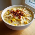 A white bowl filled with creamy chicken corn chowder, topped generously with crumbled bacon pieces.
