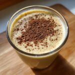 A close-up, top-down view of creamy homemade eggnog in a glass, dusted heavily with cinnamon.
