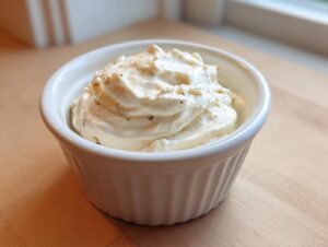 A white ramekin filled with creamy horseradish sauce for prime rib, sitting on a light wooden surface.