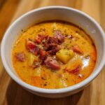 Close-up of a rich, creamy kielbasa potato soup topped with chunks of sausage and herbs.