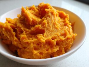 A close-up of fluffy, vibrant orange mashed sweet potatoes served in a white bowl.