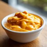 Close-up of thick, bright orange homemade nacho cheese sauce served in a small white bowl.