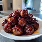 A pile of shiny, glazed Crockpot grape jelly meatballs served on a white plate.