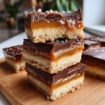 A stack of three homemade Twix bars showing the shortbread, gooey caramel, and chocolate topping.