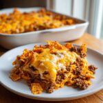A generous serving of doritos casserole with ground beef, melted cheese, and sour cream on a white plate.