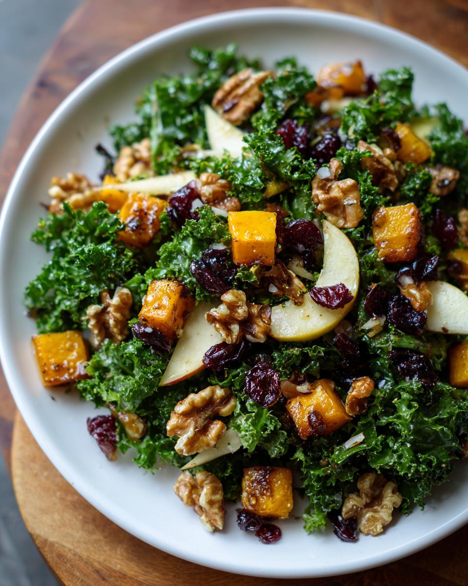 Close-up of a vibrant Fall Harvest Salad featuring kale, roasted squash cubes, walnuts, apple slices, and dried cranberries.