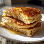 Close-up of a stack of three thick, fluffy almond flour pancakes topped with melting butter and syrup.