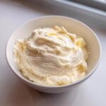 A white bowl filled with freshly whipped, fluffy cream cheese frosting, showing soft peaks.