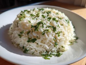 A mound of fluffy white garlic butter rice topped generously with chopped fresh green parsley on a white plate.