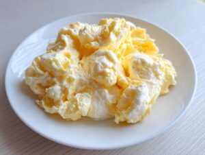 A close-up of very fluffy scrambled eggs with creamy curds served on a simple white plate.