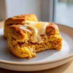 Close-up of a fluffy sweet potato biscuits, split open and topped with melting butter.