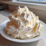 A large, fluffy mound of freshly made vanilla buttercream frosting piled high on a white plate.
