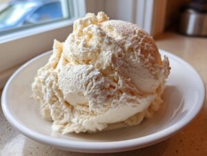 A large, fluffy scoop of pale yellow vanilla buttercream frosting served in a small white bowl.