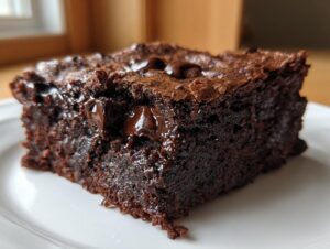 A close-up, decadent square of fudgy brownies featuring a shiny, crackly top and gooey, melted chocolate chips inside.