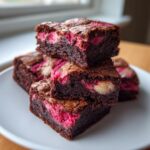 Close-up of stacked, fudgy strawberry brownies featuring vibrant pink swirls and a crackly top.