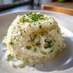 A perfectly molded serving of fluffy garlic butter rice topped generously with fresh chopped parsley.