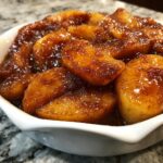 Thick, glossy, cinnamon-spiced apple pie filling slices served warm in a white bowl.