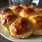 A cluster of freshly baked, golden brown homemade dinner rolls with a shiny glaze on a white plate.