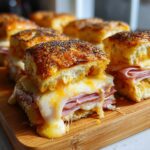 Close-up of gooey Ham and Cheese Sliders with melted cheese dripping over layers of ham on poppy seed buns.