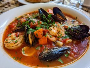 Close-up of a bowl of rich, tomato-based seafood soup featuring mussels, shrimp, and chopped vegetables.