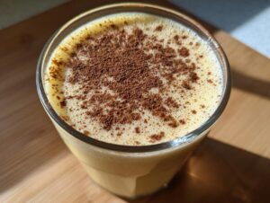 Close-up of a glass of creamy, frothy homemade eggnog topped with a dusting of cinnamon or nutmeg.