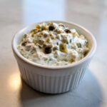 Close-up of creamy homemade tartar sauce recipe, topped with capers and relish, served in a small white bowl.