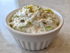 Close-up of creamy homemade tartar sauce recipe with visible relish, capers, and lemon zest in a white bowl.